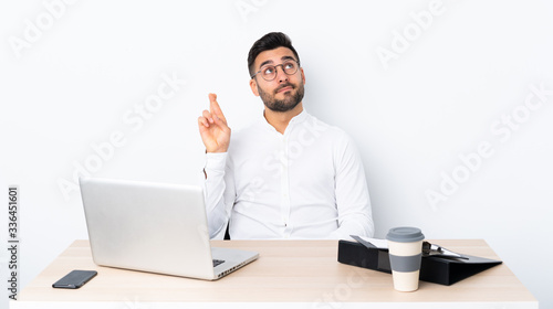 Young businessman in a workplace with fingers crossing and wishing the best