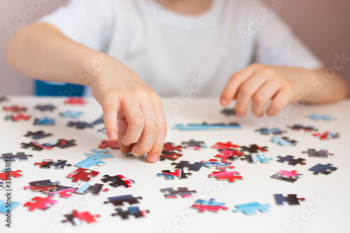 The child collects a puzzle. Elements of the puzzle are laid out on a white table. Children's hands during the game. Home leisure.