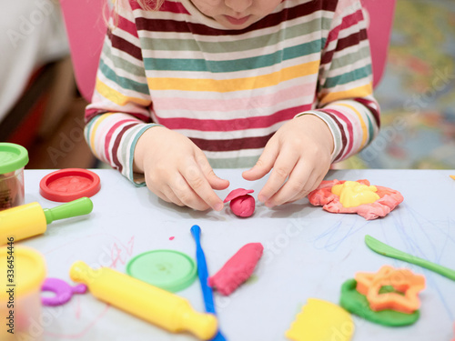 Child hands playing with colorful clay. Plasticine. play dough, social distance quarantine Covid-19, self-isolation, online education concept, homeschooling. Toddler girl at home, kindergarden closed.