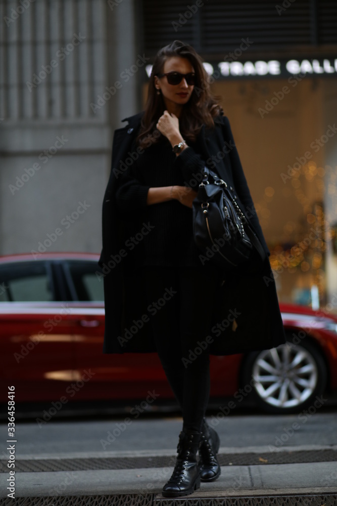 Fototapeta premium A beautiful woman in a black long coat walks through the streets of New York