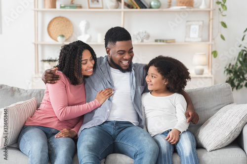 Loving Black Man Embracing Wife And Daughter On Couch At Home