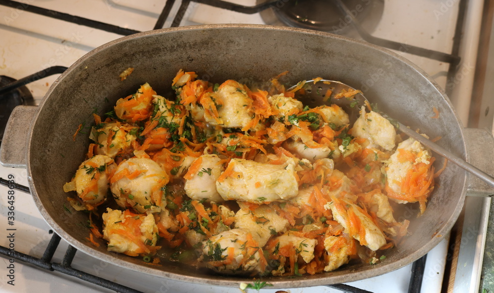 Chunks of white meat with carrots and herbs in a cast-iron pot on the stove. Photographed in room light through steam coming from a pot. Chunks of white meat with carrots and herbs in a cast-iron pot on the stove. Photographed in room light through steam coming from a pot.