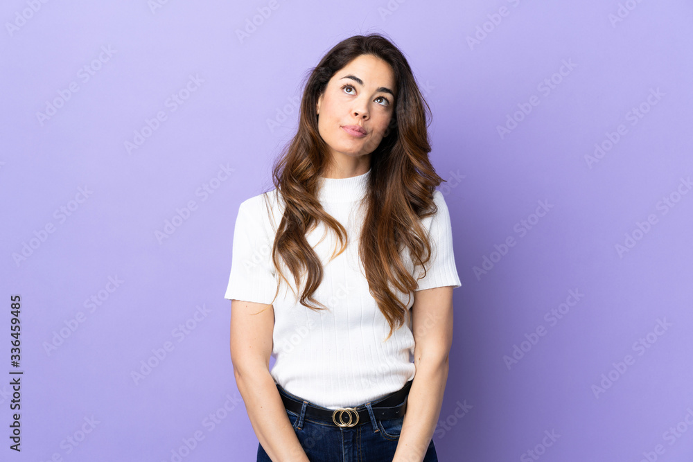 Woman over isolated purple background having doubts while looking up Woman over isolated purple background having doubts while looking up