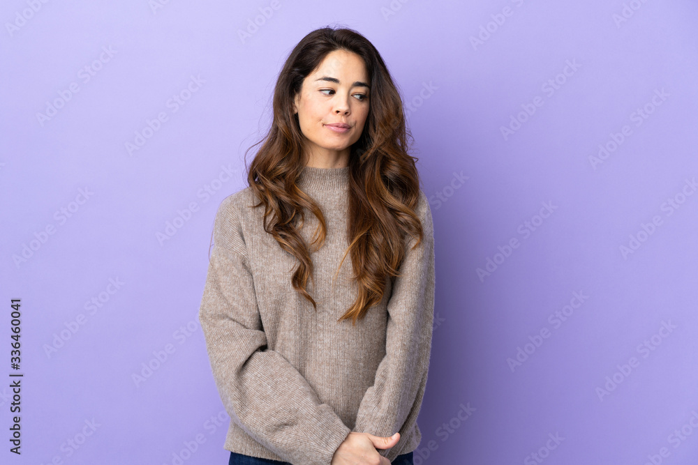 Woman over isolated purple background having doubts while looking side Woman over isolated purple background having doubts while looking side