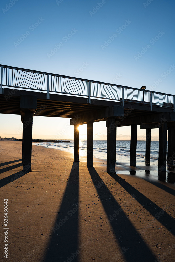 Sunrise over Atlantic Ocean with blue clear sky, blue ocean, wooden pier, birds flying over sunrise red sky beams
