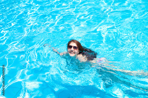 Portrait of a smiling beautiful girl wearing sunglasses in the pool on a summer day. Resort