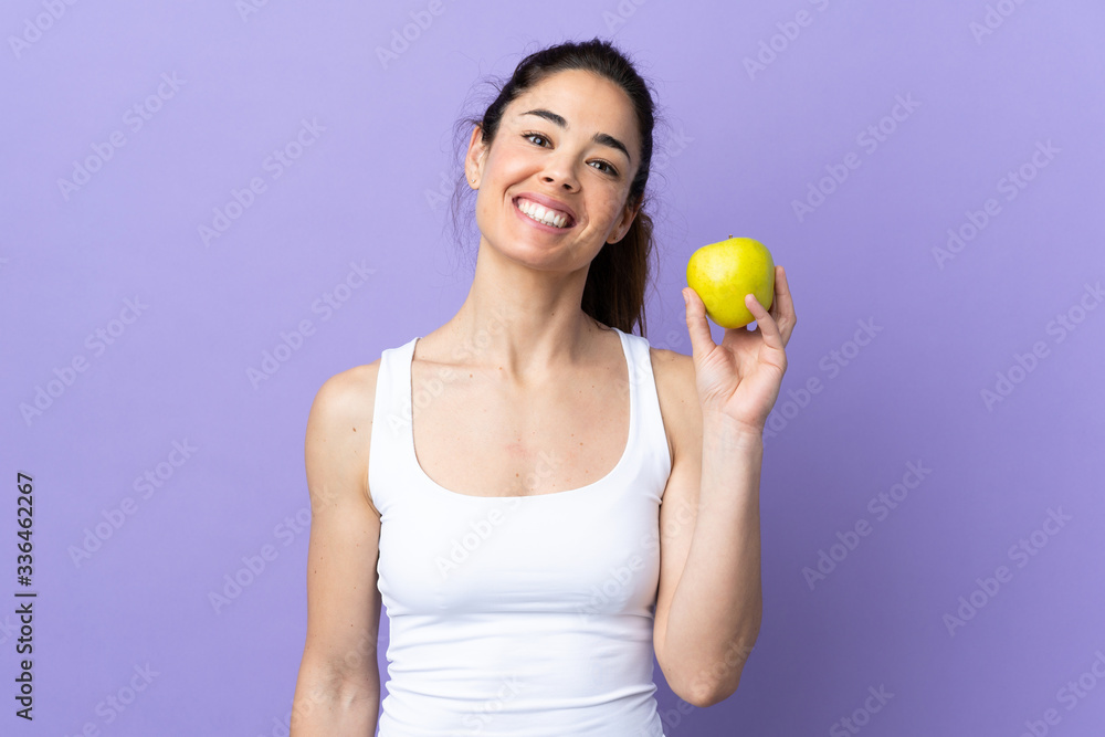 Woman over isolated purple background with an apple and happy Woman over isolated purple background with an apple and happy