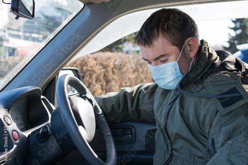 A young man in a car wearing a medical mask lowered his head, feeling ill. © Инесса Гревцова