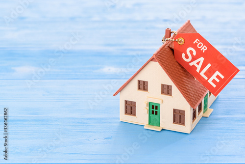 Affordable existing house for sale / reverse mortgage, financial concept : Model home with a tag for sale on wood background, depicts selling asset or changing property to cash for personal expense