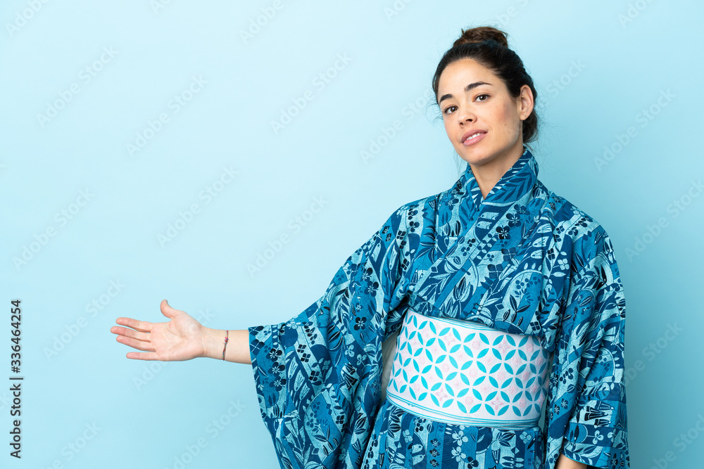 Woman wearing kimono over isolated background extending hands to the side for inviting to come Woman wearing kimono over isolated background extending hands to the side for inviting to come