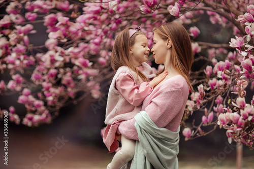 Happy family mother and daughter in pink clothes in the spring in a flowered park for a walk. a woman holds a baby in her arms, they look at each other