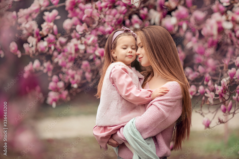 Happy family mother and daughter in pink clothes in the spring in a flowered park for a walk. woman holding a baby in her arms, they closed their eyes and dream