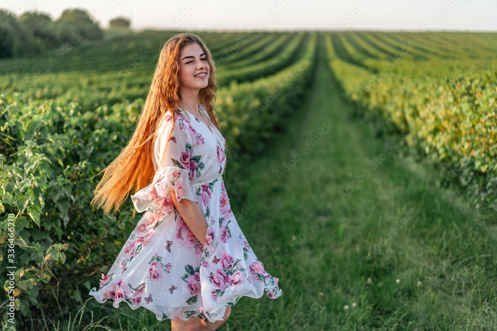 beautiful woman with long curly hair and freckles face on currant field background. Girl in a light dress walks in the summer sunny day beautiful woman with long curly hair and freckles face on currant field background. Girl in a light dress walks in the summer sunny day