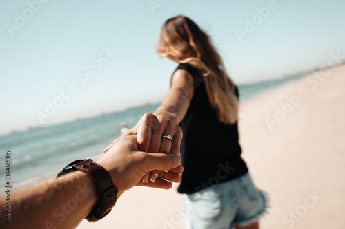 Fresh engaged couple enjoying a romantic engagement day on the beach during a sunny day. Close up on her ring.