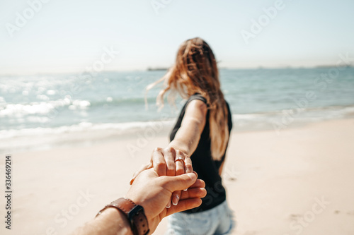 Fresh engaged couple enjoying a romantic engagement day on the beach during a sunny day. Close up on her ring.