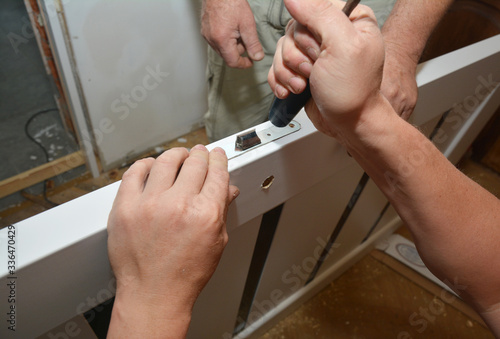 Tableau sur toile Building contractor is installing mortise lock into a bathroom door, fitting a lock into a door gently tapping it