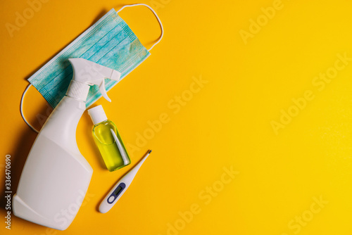 Medical face protection mask, alcohol antiseptic, disinfectant liquid, thermometer on a yellow background with place for text, the concept of the fight against coronavirus