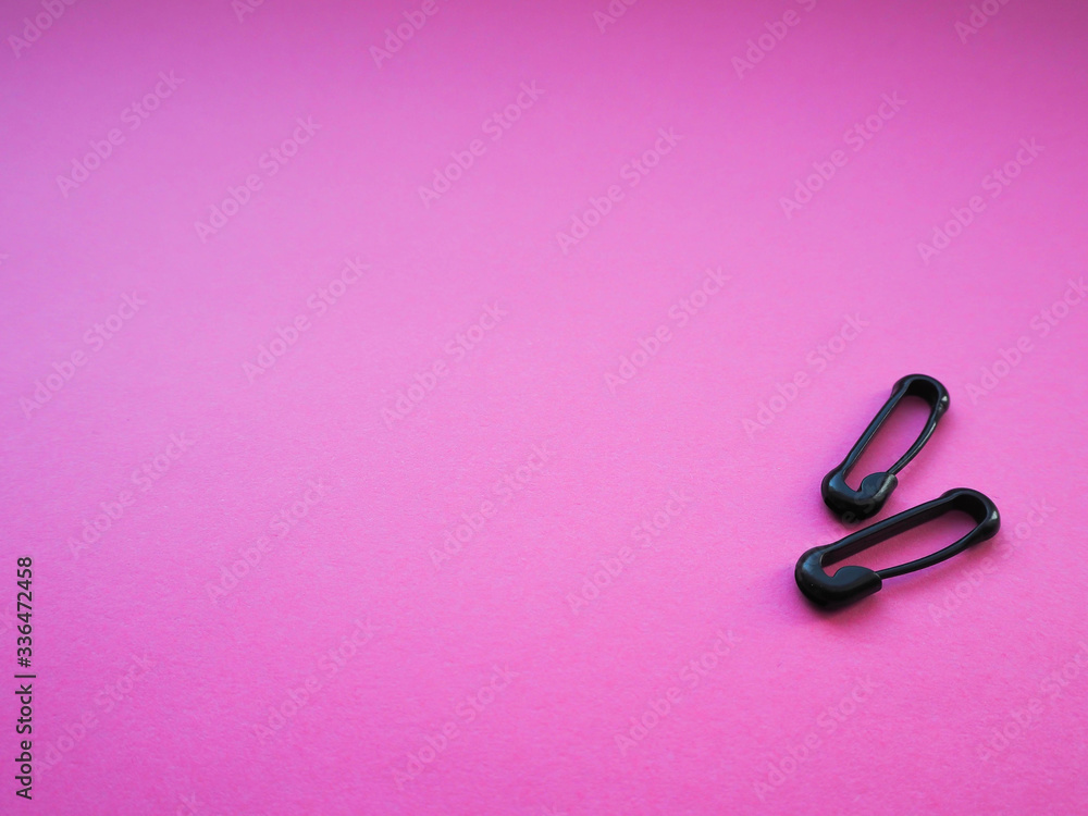 two black closed safety pins on a bright pink background two black closed safety pins on a bright pink background