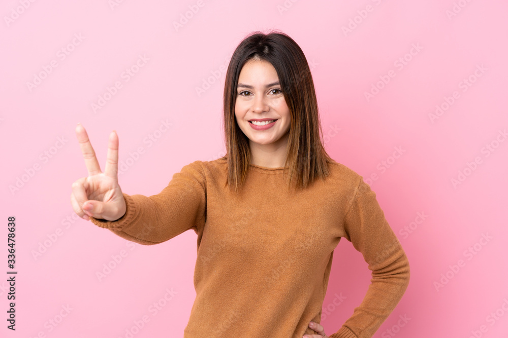 Young woman over isolated pink background smiling and showing victory sign Young woman over isolated pink background smiling and showing victory sign
