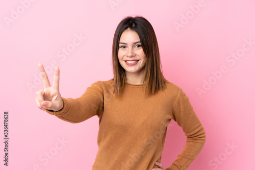 Young woman over isolated pink background smiling and showing victory sign © luismolinero