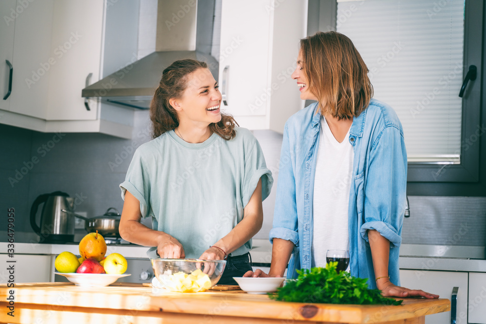 Two young beautiful women girlfriends lesbian couple cook at home in the kitchen cuddling and laughing merrily, home activism, cooking, recipes, staying at home Two young beautiful women girlfriends lesbian couple cook at home in the kitchen cuddling and laughing merrily, home activism, cooking, recipes, staying at home