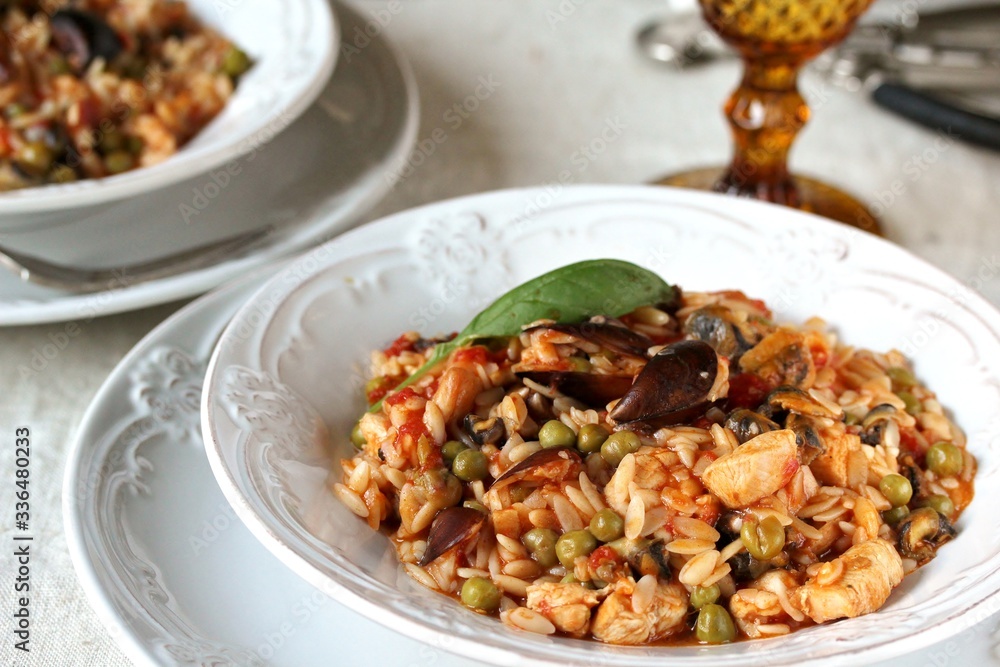 paella from orzo pasta with mussels, seashells and chicken. Seafood paella, traditional spanish dish. Paella on rustic black wooden table. Top view paella from orzo pasta with mussels, seashells and chicken. Seafood paella, traditional spanish dish. Paella on rustic black wooden table. Top view