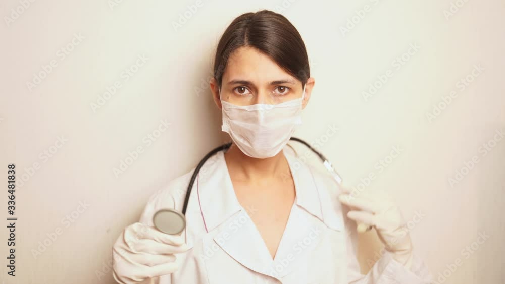 a female doctor in a white disposable protective mask and disposable gloves takes out a stethoscope and prepares to listen to the patient a female doctor in a white disposable protective mask and disposable gloves takes out a stethoscope and prepares to listen to the patient
