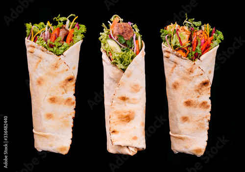Delicious turkish doner kebab with chicken,lamb,beef grilled, onion, tomatoes, lettuce, parsley, carrot,  cucumbers and sauce isolated on black background 