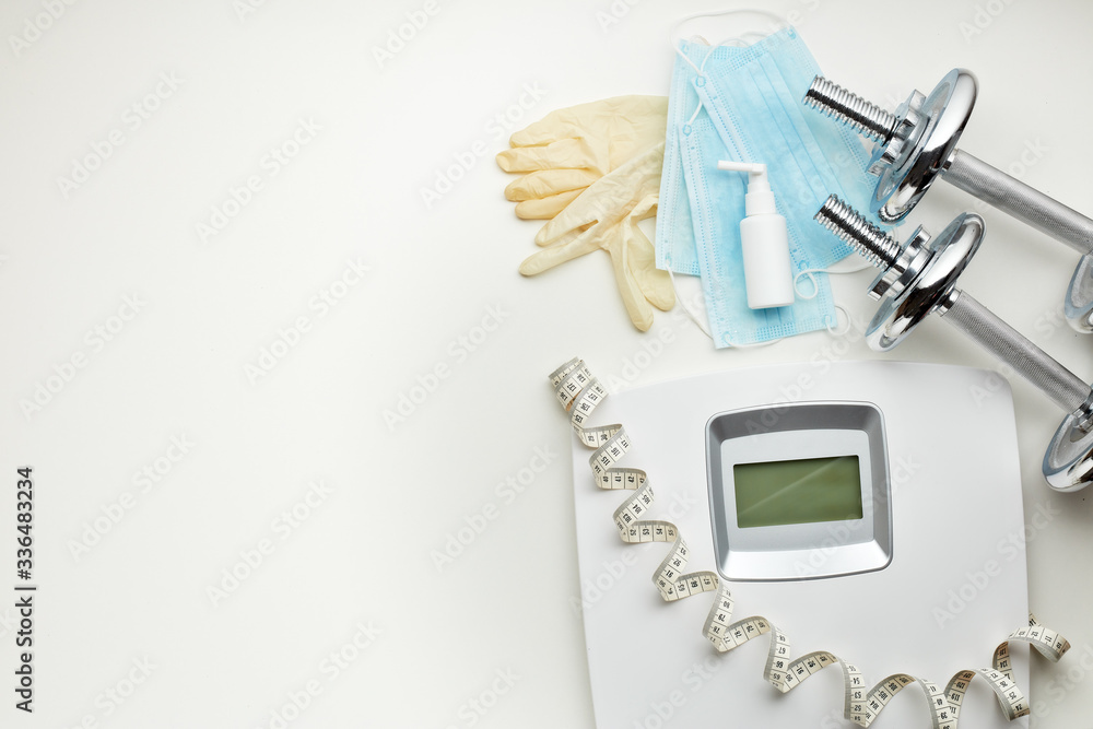 Sport equipment, scales, medical masks and sanitizer on white background. Fitness. Weight and health control during quarantine.