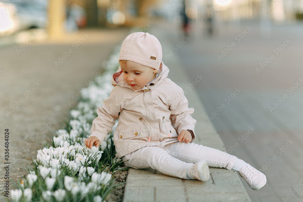 A girl in pink clothes plays with spring-blooming crocuses.