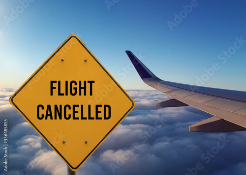 Yellow warning metal sign with Flight Cancelled text and the wing of the plane on beautiful blue cloudy background. Coronavirus caused flight cancellations and crisis of travelling industry concept