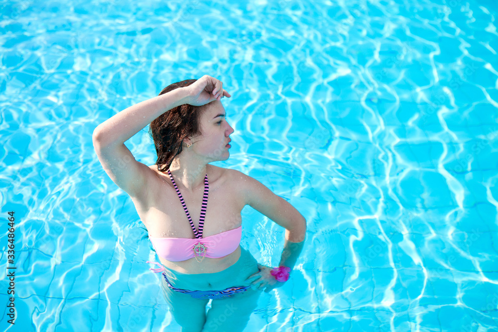 Young beautiful girl in a pink bathing suit posing in a pool with blue water. Travel resort