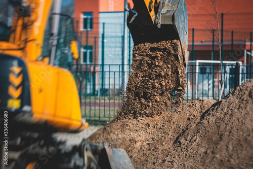 Yellow heavy excavator excavating sand and working during road works, unloading sand during construction of the new road with workers around