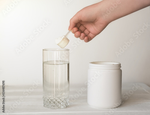 hand holding scoop of fish collagen. collagen peptides in container or jar. glass of water for mixing drink. Healthcare supplement concept. collagen powder for skin and joints .