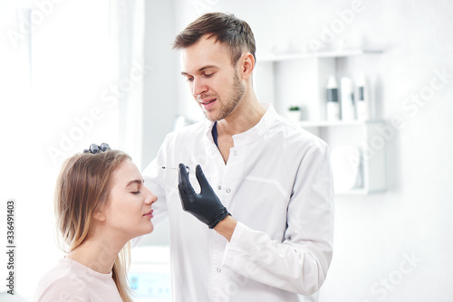 Beautician man gives beauty injections to young woman patient, handsome dermatologist puts disport in forehead wrinkles, face botox filler in the cosmetology salon