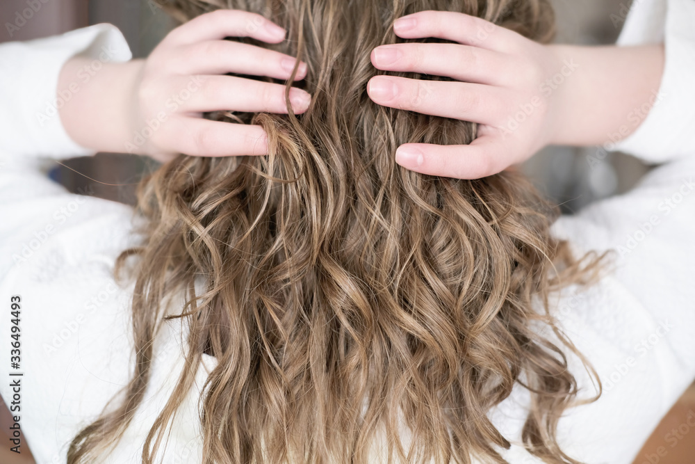 Naklejka premium teenage girl with natural wavy hair. blond girl touching her hair, back view. natural curly no brush method for beautiful stylish look. trendy messy style.