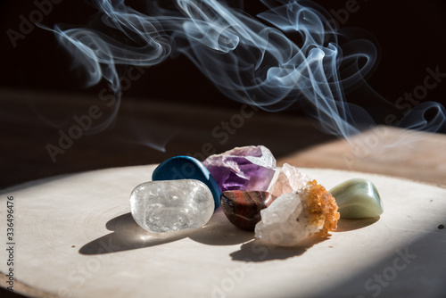 Mineral stones on the wooden plate with smoke in the background during beautiful morning light indoor. Cleansing and purifying the energy and vibe indoor. Part of meditation, therapy, aromatherapy. 