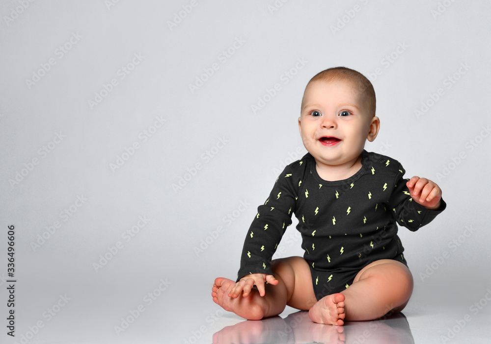 Little toddler in black bodysuit, barefoot. He is smiling while sitting on floor isolated on white studio background. Close up Little toddler in black bodysuit, barefoot. He is smiling while sitting on floor isolated on white studio background. Close up