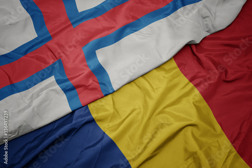 waving colorful flag of romania and national flag of faroe islands.