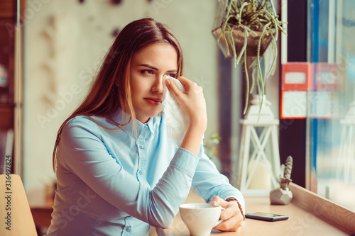 Misery, infelicity. Brunette woman girl about to cry wiping tears sneezing in a tissue drinking tea, coffee, hot beverage. Negative human emotion, face expression, reaction, body language photo