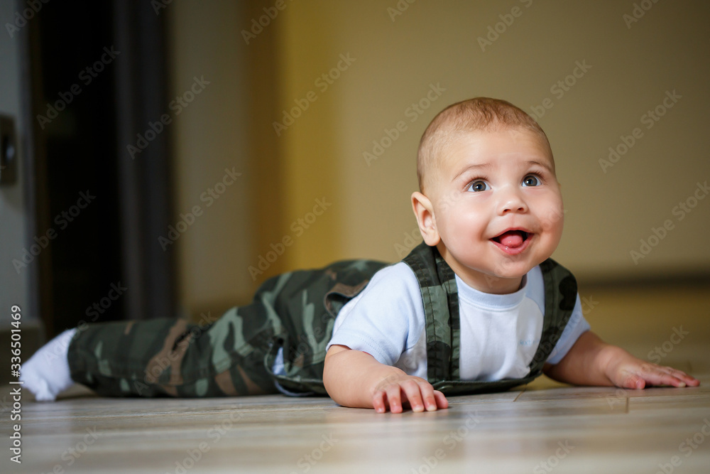 little boy aged 8 months in overalls, a white shirt and white socks crawling on the floor and smiling little boy aged 8 months in overalls, a white shirt and white socks crawling on the floor and smiling