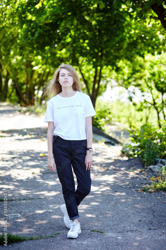 Beautiful attractive woman in white t-shirt posing in the summer park. Active smiling girl resting outdoors Beautiful attractive woman in white t-shirt posing in the summer park. Active smiling girl resting outdoors