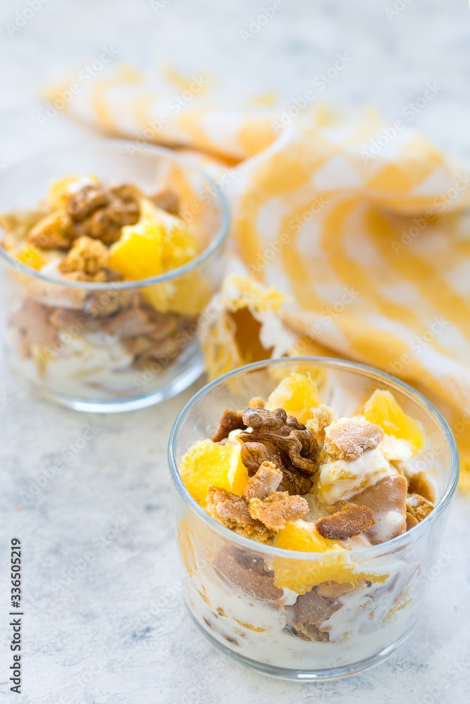 Dessert laid out in layers from pieces of cookies, fruits and cream, decorated with nuts in glass glasses on a light background, vertical arrangement Dessert laid out in layers from pieces of cookies, fruits and cream, decorated with nuts in glass glasses on a light background, vertical arrangement