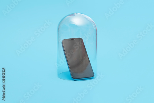 Mobile smartphone in quarantine under a glass cloche dome on a blue background with copy space and room for text