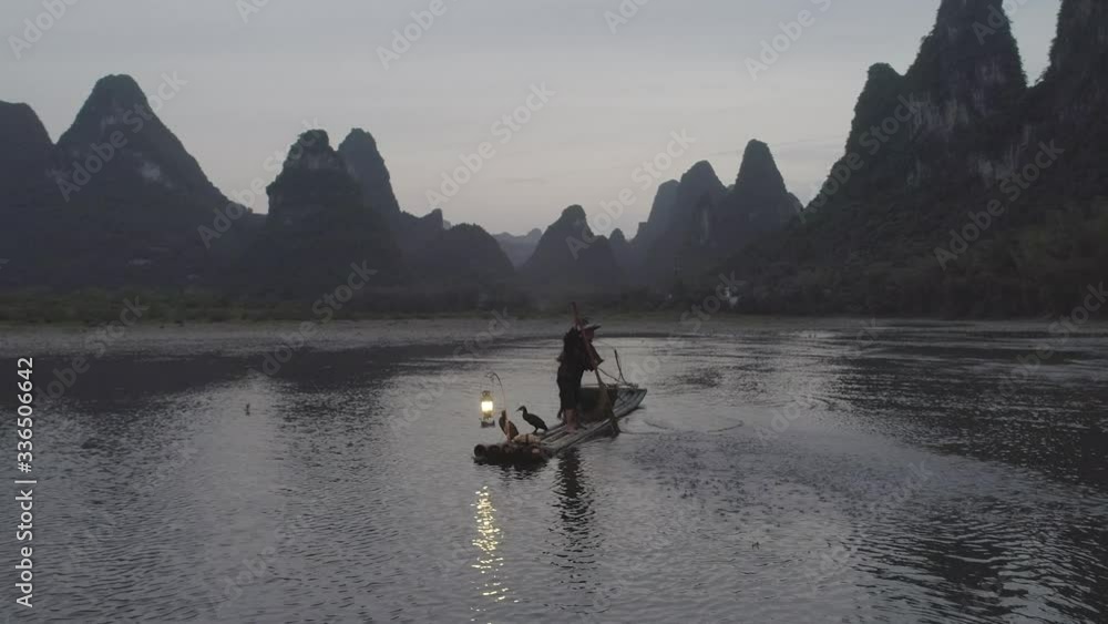 Slow moving panning arial shot of Chinese cormorant fisherman punting a bamboo raft across a broad expanse of water with karst towers in the background Slow moving panning arial shot of Chinese cormorant fisherman punting a bamboo raft across a broad expanse of water with karst towers in the background