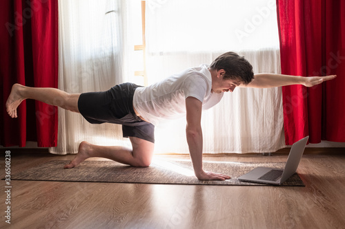 Obraz na plátně Man practices yoga asana chakravakasana or bird pose at the living room