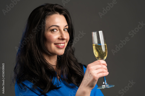 Attractive latin mature woman smiling and holding glass of champagne or wine on grey studio background. Drinking alcohol concept