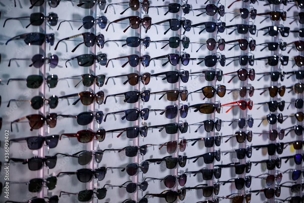 Fototapeta premium A row of glasses to protect from the sun. Store points. Stand with sunglasses in the optics store. Female hand shows glasses. Presentation of points. Close-up
