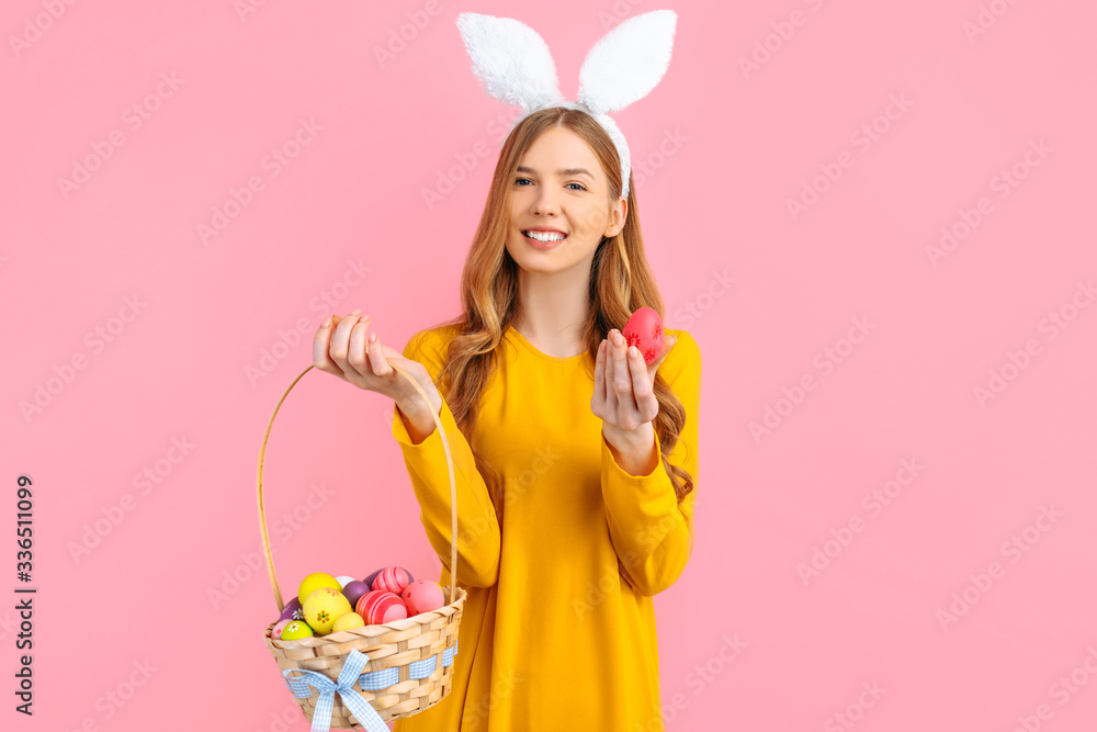 Happy Easter. happy young woman wears rabbit ears on Easter day and holds a basket of Easter eggs, on an isolated pink background Happy Easter. happy young woman wears rabbit ears on Easter day and holds a basket of Easter eggs, on an isolated pink background