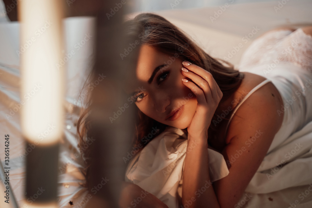 Portrait of a hot and graceful woman laying in a white lace lingerie among bed sheets, star-shaped confetti and holding her pillow Portrait of a hot and graceful woman laying in a white lace lingerie among bed sheets, star-shaped confetti and holding her pillow